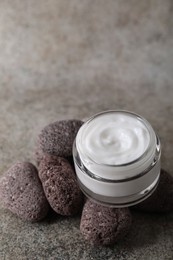 Photo of Face cream in jar and stones on grey textured table, closeup. Space for text