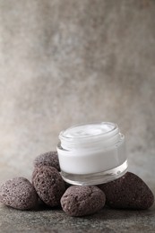 Photo of Face cream in jar and stones on grey textured table. Space for text