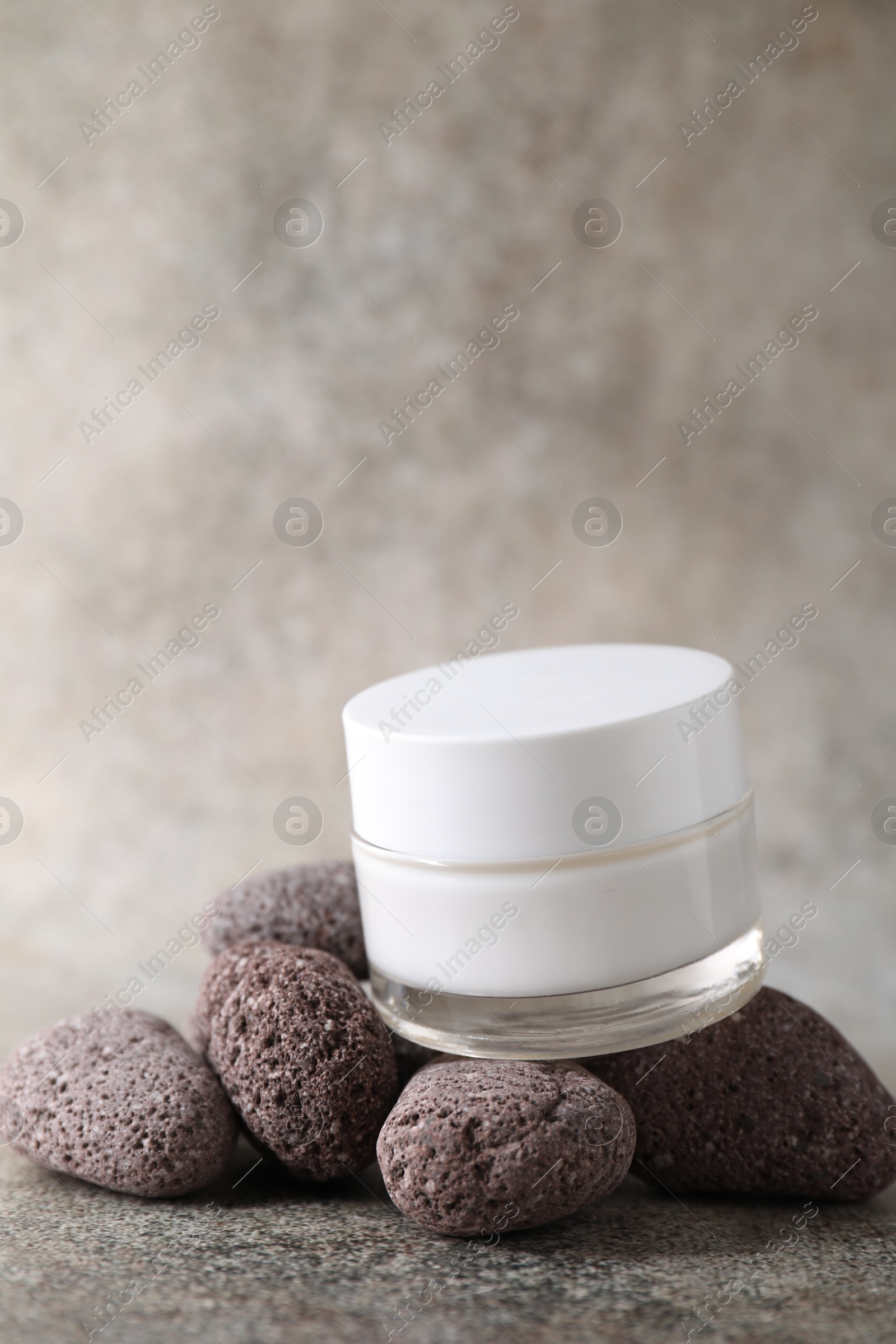 Photo of Face cream in jar and stones on grey textured table. Space for text