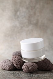 Face cream in jar and stones on grey textured table. Space for text