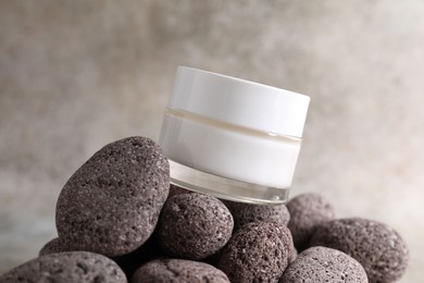 Photo of Face cream in jar and stones on blurred background, closeup