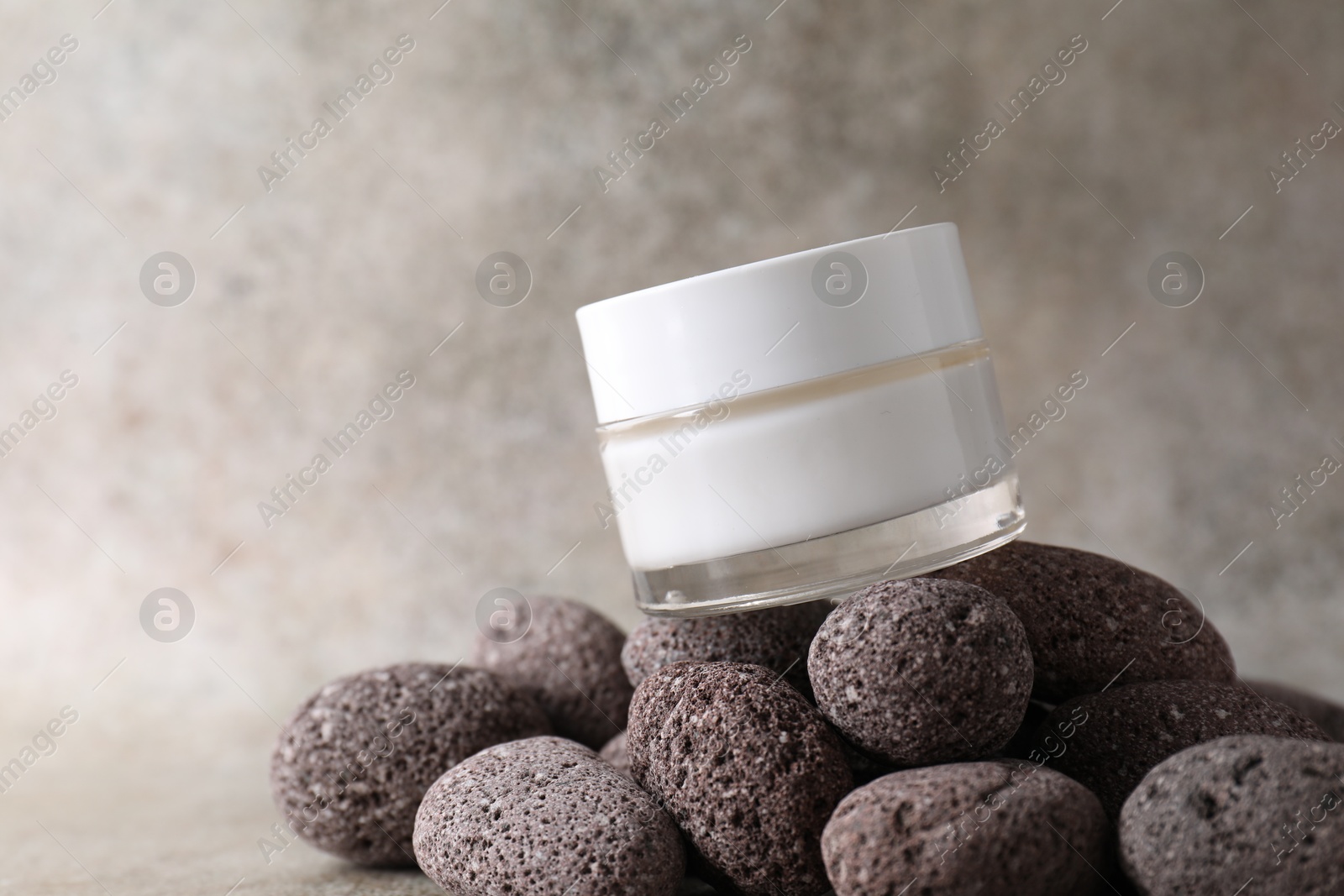 Photo of Face cream in jar and stones on blurred background, closeup. Space for text