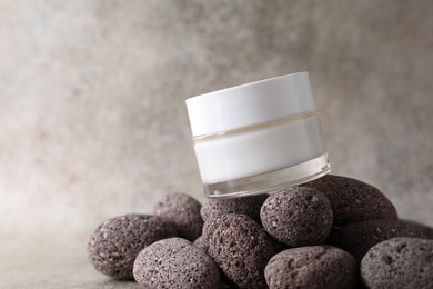 Face cream in jar and stones on blurred background, closeup. Space for text