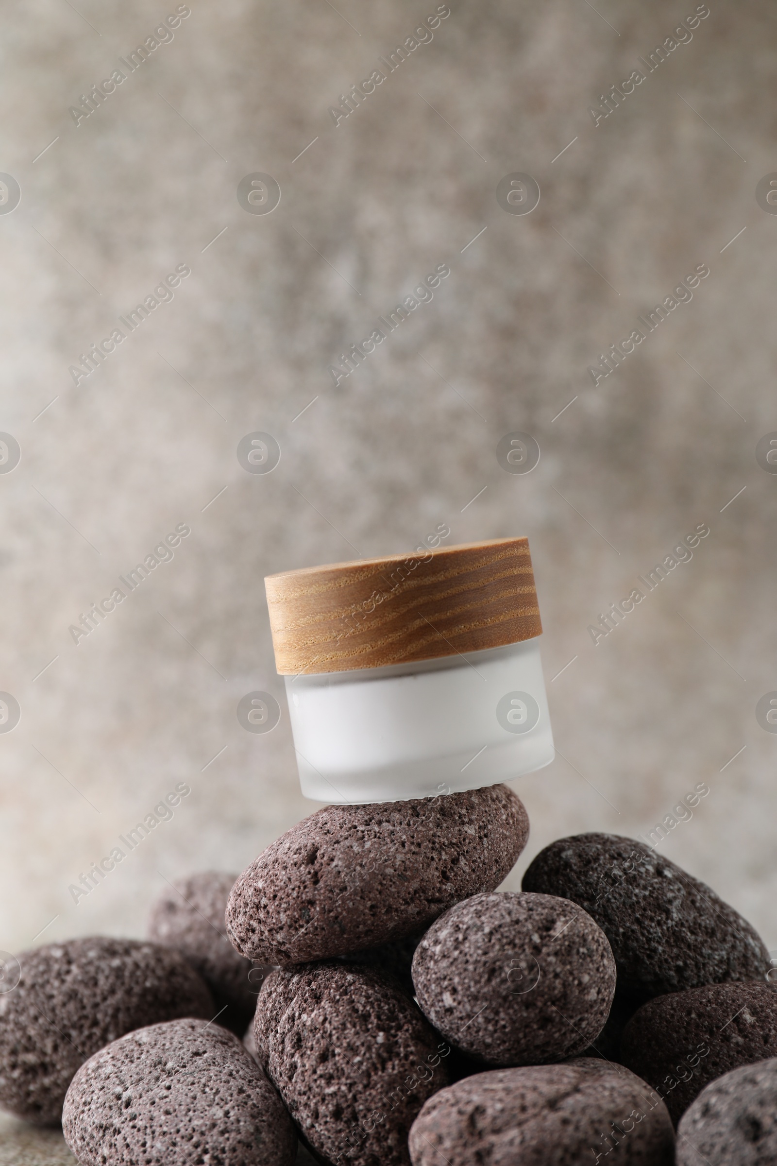 Photo of Face cream in jar and stones on blurred background, closeup. Space for text