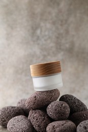 Face cream in jar and stones on blurred background, closeup. Space for text