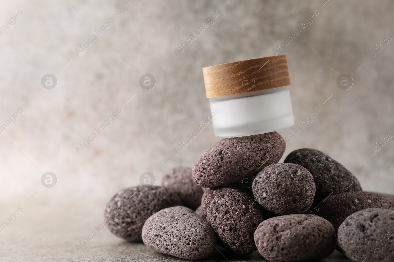 Photo of Face cream in jar and stones on blurred background, closeup. Space for text