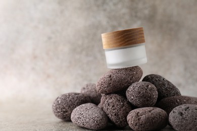 Face cream in jar and stones on blurred background, closeup. Space for text