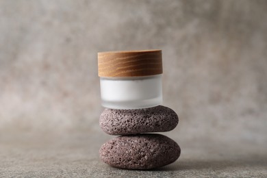 Photo of Face cream in jar and stones on grey textured table, closeup