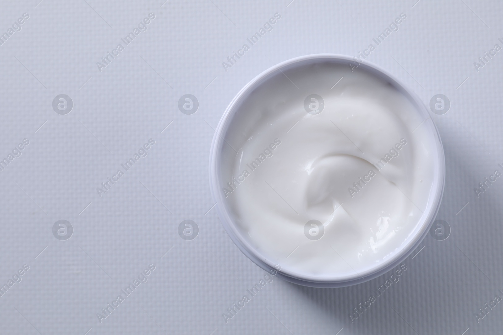 Photo of Face cream in jar on white textured table, top view. Space for text