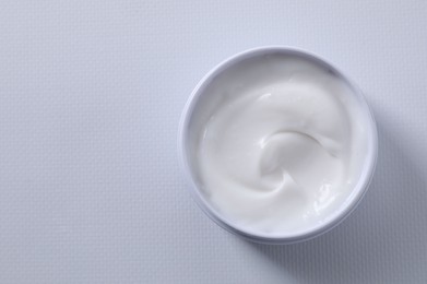 Face cream in jar on white textured table, top view. Space for text