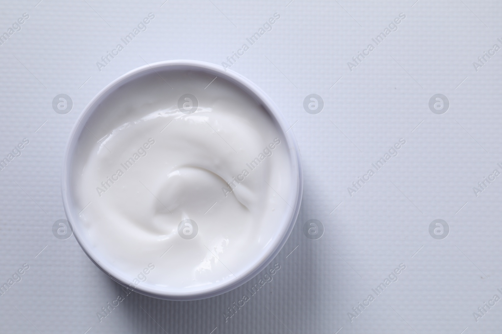 Photo of Face cream in jar on white textured table, top view. Space for text