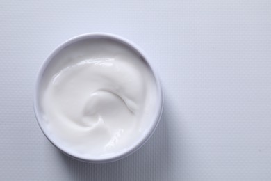 Face cream in jar on white textured table, top view. Space for text