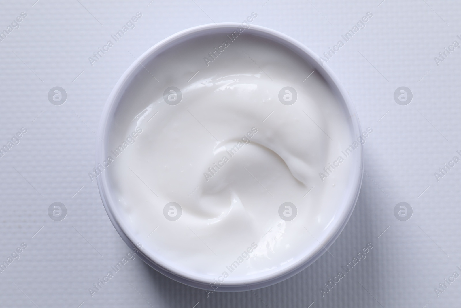 Photo of Face cream in jar on white textured table, top view