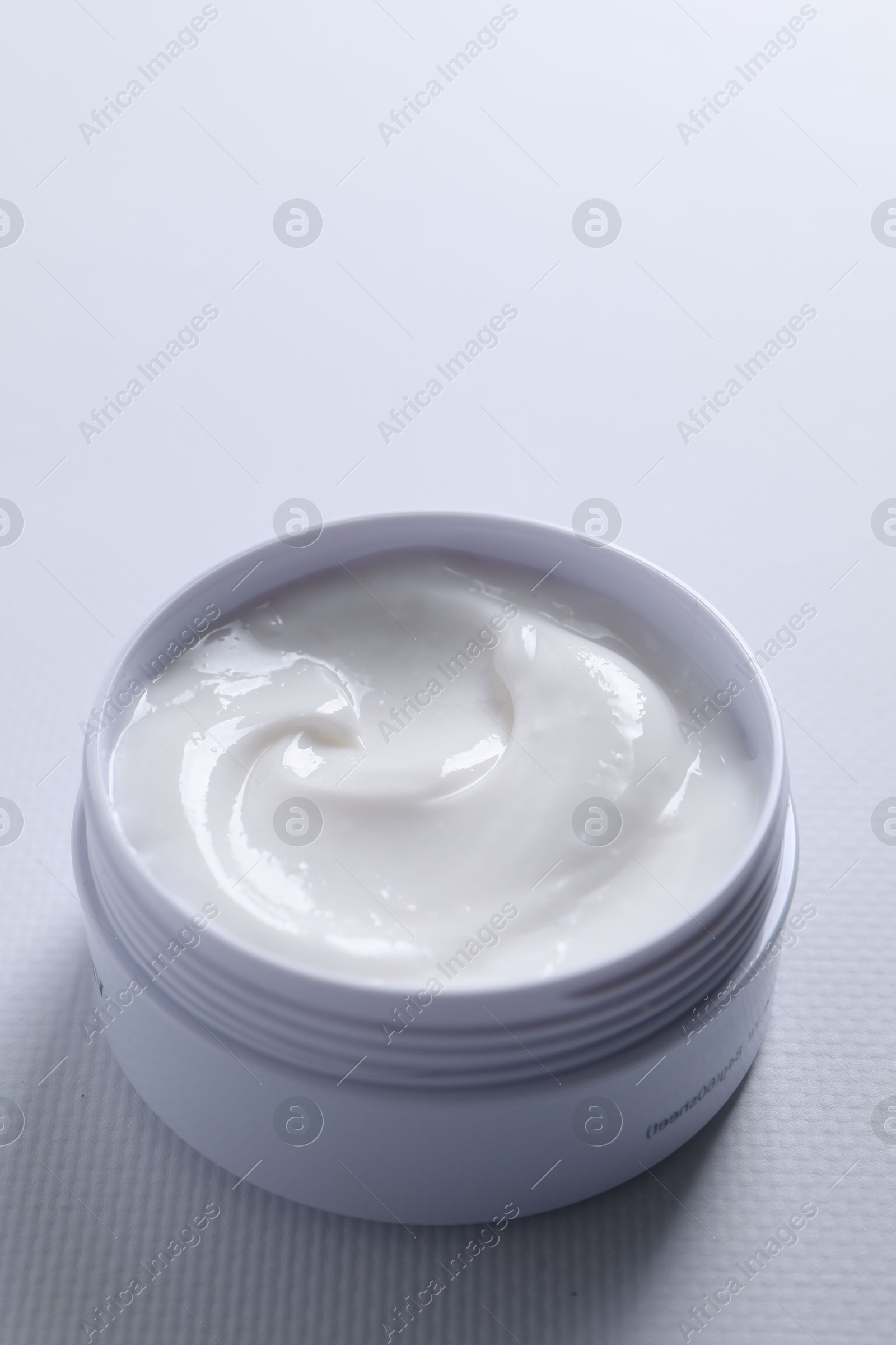 Photo of Face cream in jar on white textured table, closeup