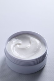 Photo of Face cream in jar on white textured table, closeup