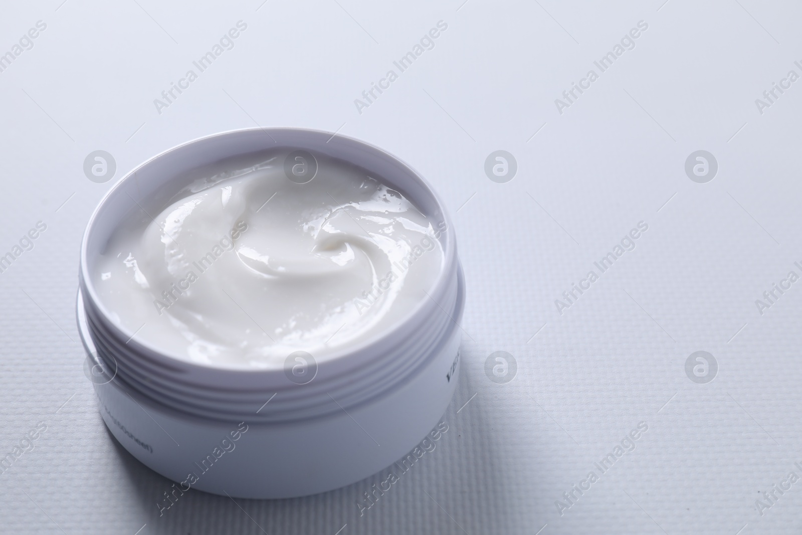 Photo of Face cream in jar on white textured table, closeup. Space for text