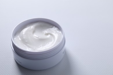 Face cream in jar on white textured table, closeup. Space for text