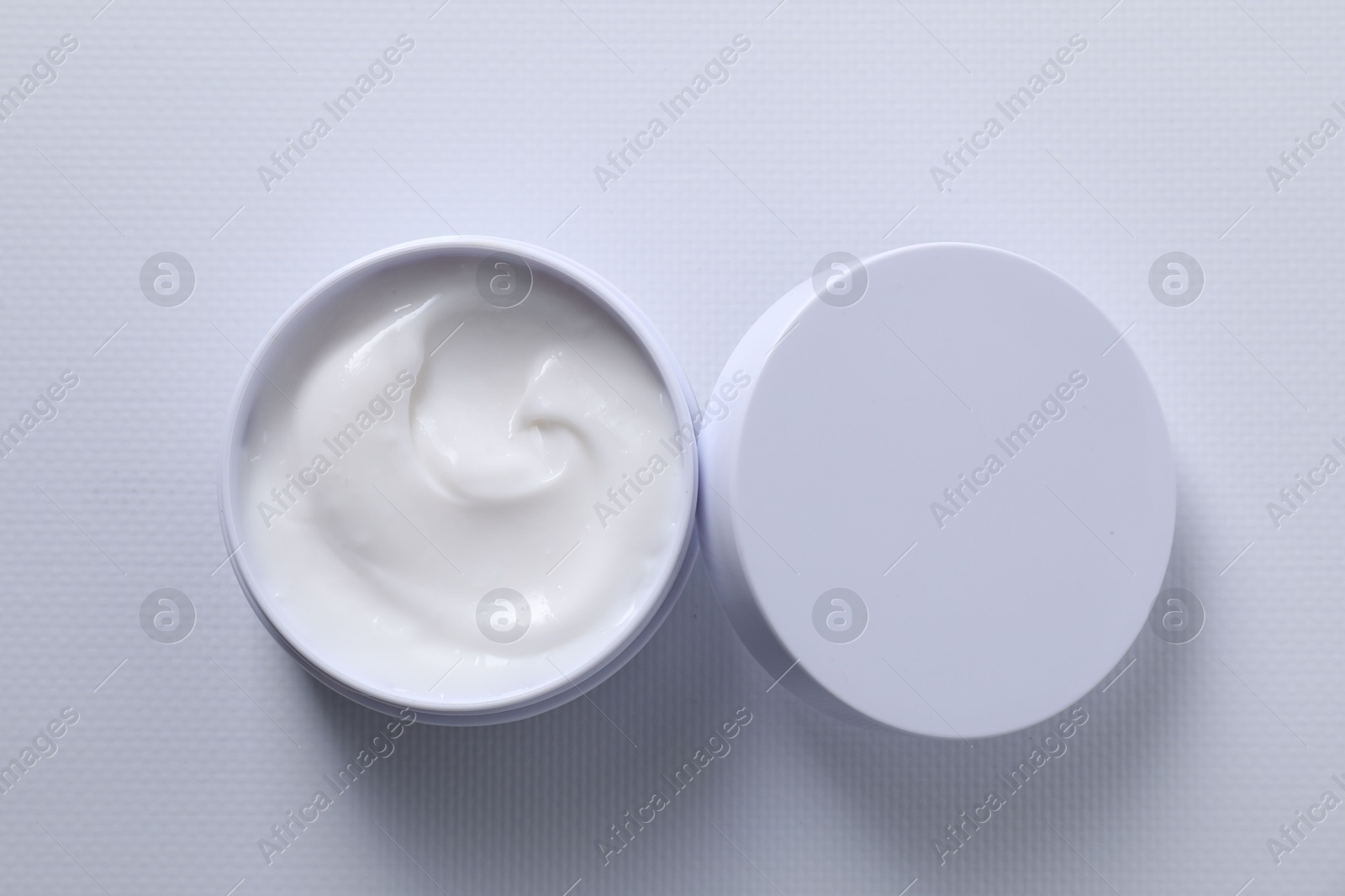 Photo of Face cream in jar on white textured table, top view