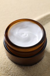 Photo of Face cream in jar on beige textured background, closeup