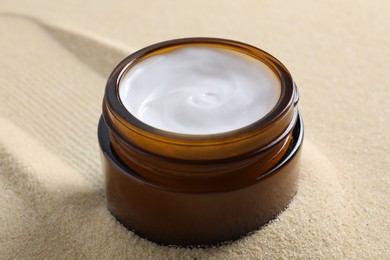 Photo of Face cream in jar on beige textured background, closeup