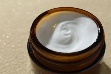 Face cream in jar on beige textured background, closeup