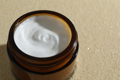 Face cream in jar on beige textured background, closeup. Space for text