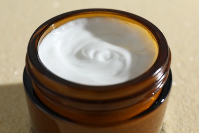 Photo of Face cream in jar on beige textured background, closeup