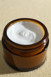 Photo of Face cream in jar on beige textured background, closeup