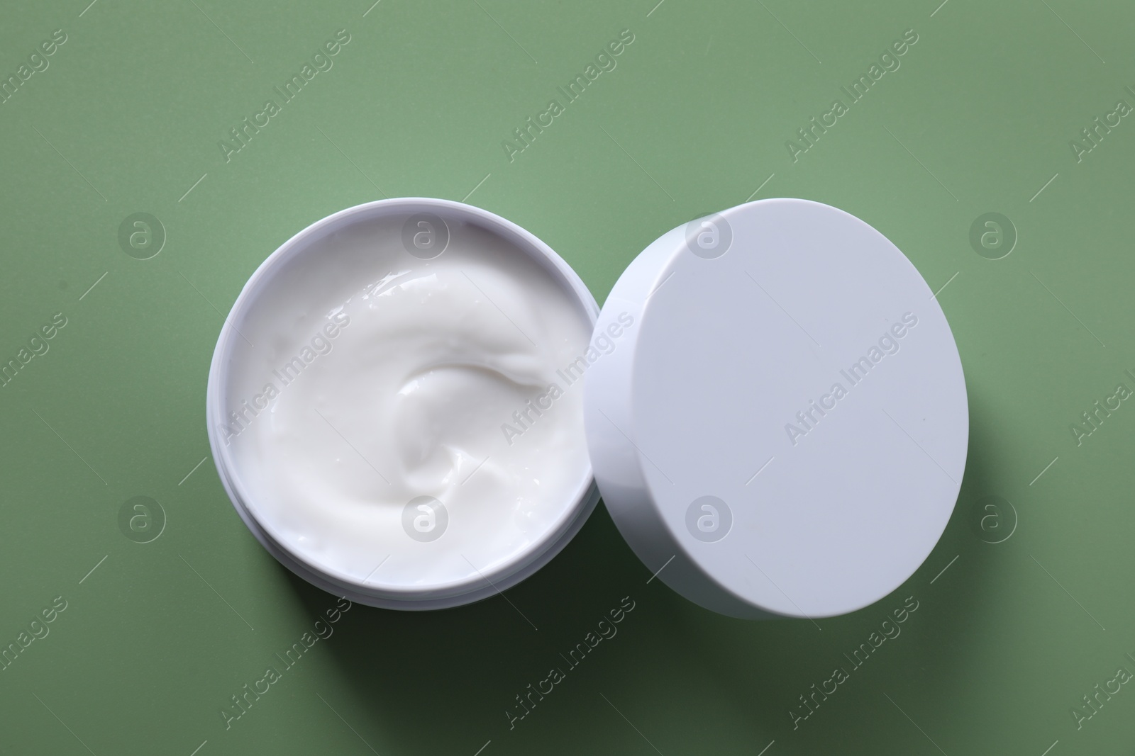 Photo of Face cream in jar on green background, top view