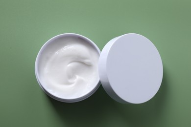 Face cream in jar on green background, top view