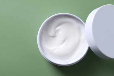 Face cream in jar on green background, top view