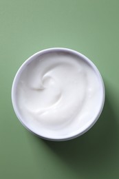 Face cream in jar on green background, top view