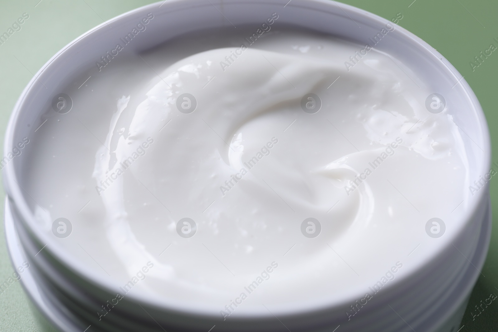 Photo of Face cream in jar on green background, closeup