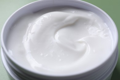 Face cream in jar on green background, closeup