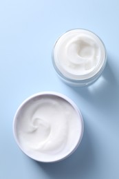 Face cream in jars on light blue background, flat lay