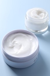 Face cream in jars on light blue background, closeup