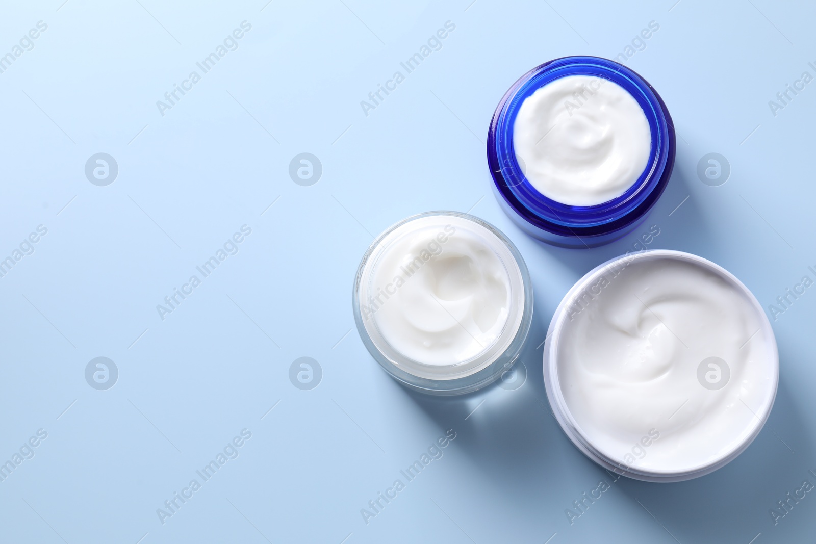 Photo of Face cream in jars on light blue background, flat lay. Space for text