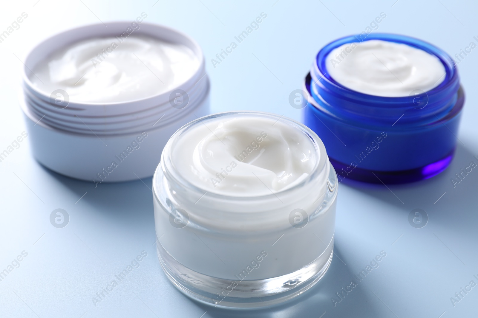 Photo of Face cream in jars on light blue background, closeup