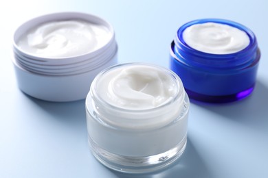 Face cream in jars on light blue background, closeup