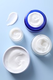 Face cream in jars on light blue background, flat lay