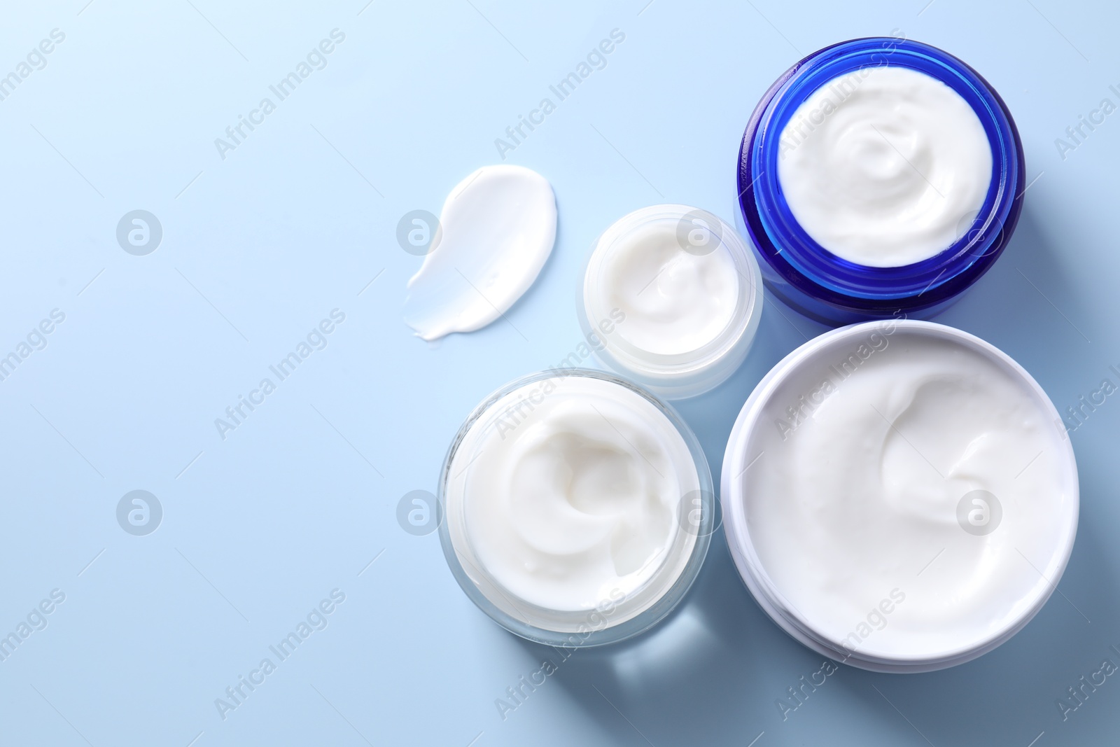 Photo of Face cream in jars on light blue background, flat lay. Space for text