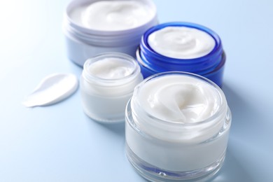 Face cream in jars on light blue background, closeup