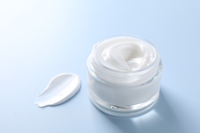 Face cream in jar and smear on light blue background, closeup