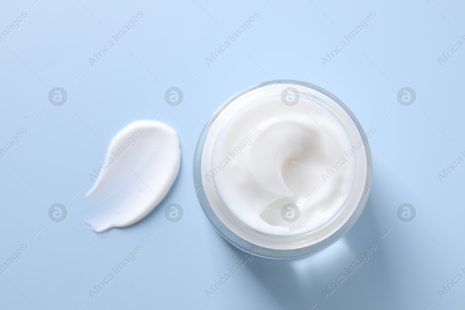 Photo of Face cream in jar and smear on light blue background, top view