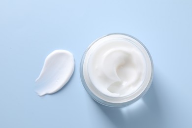 Face cream in jar and smear on light blue background, top view