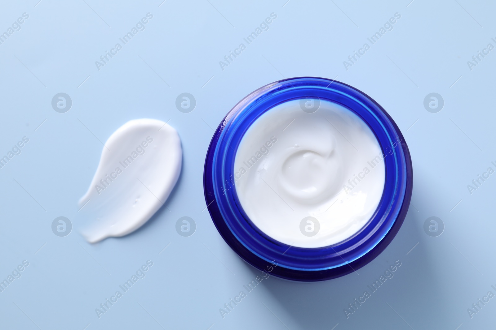 Photo of Face cream in jar and smear on light blue background, top view