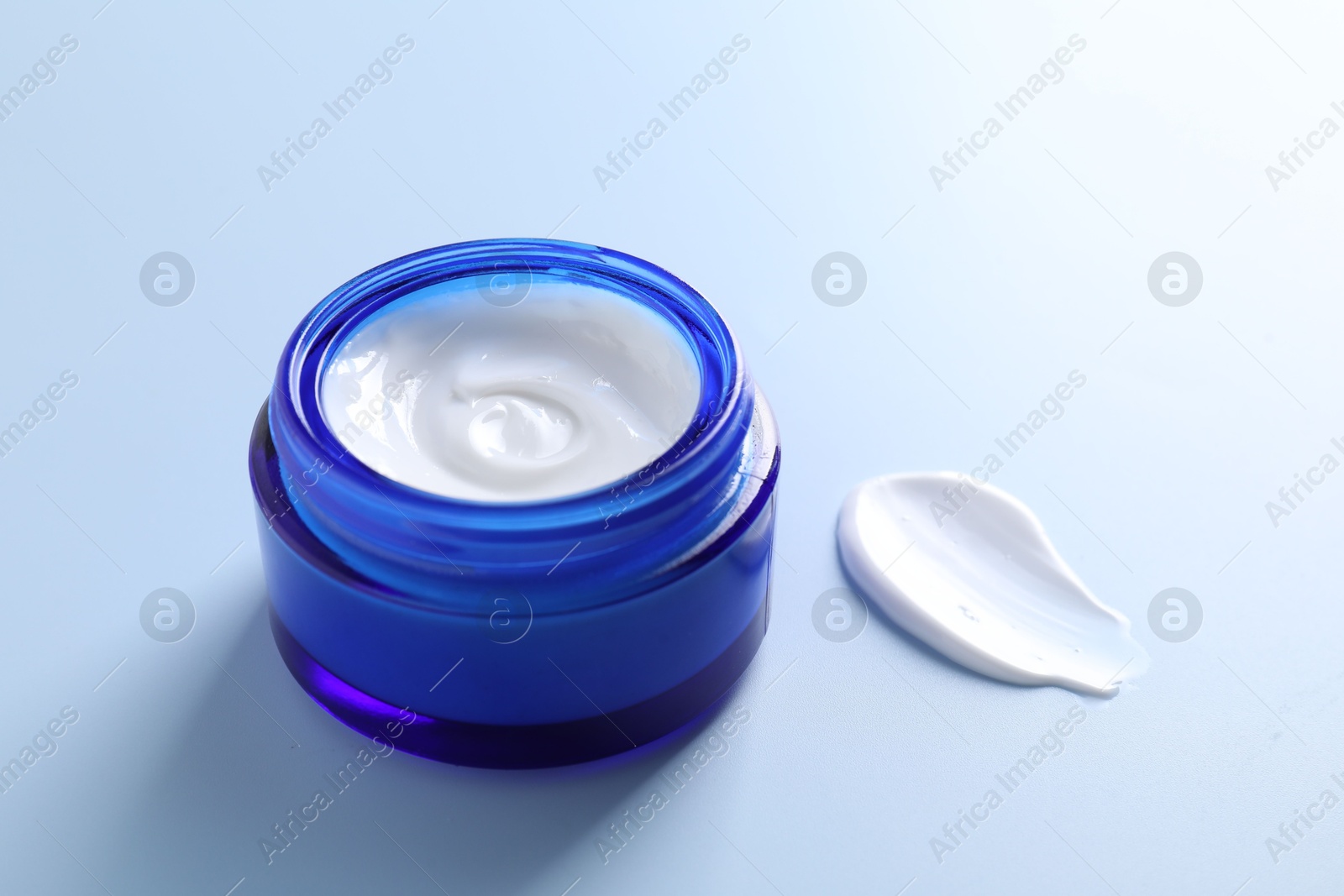 Photo of Face cream in jar and smear on light blue background, closeup