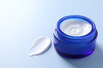 Photo of Face cream in jar and smear on light blue background, closeup. Space for text