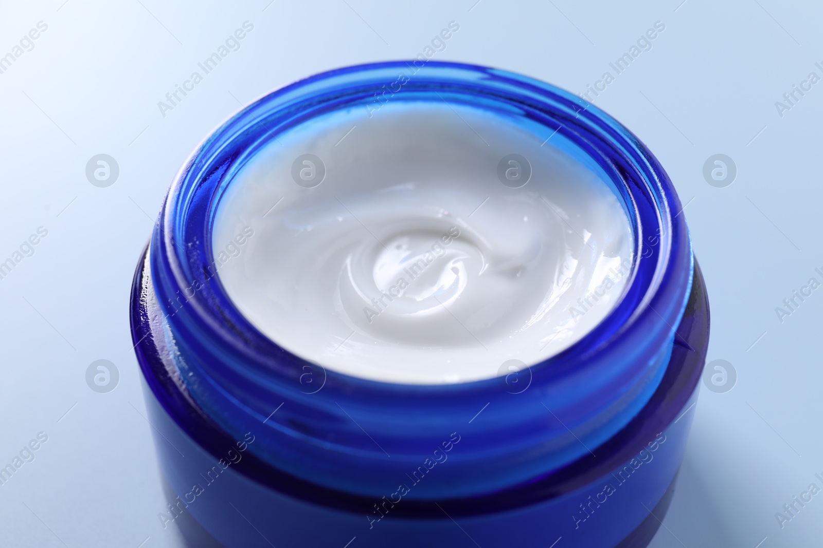 Photo of Face cream in jar on light blue background, closeup