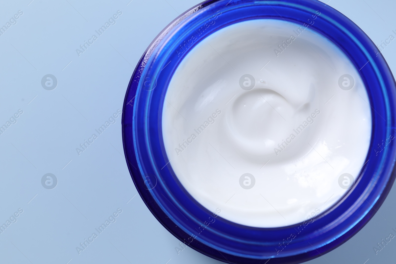 Photo of Face cream in jar on light blue background, top view. Space for text